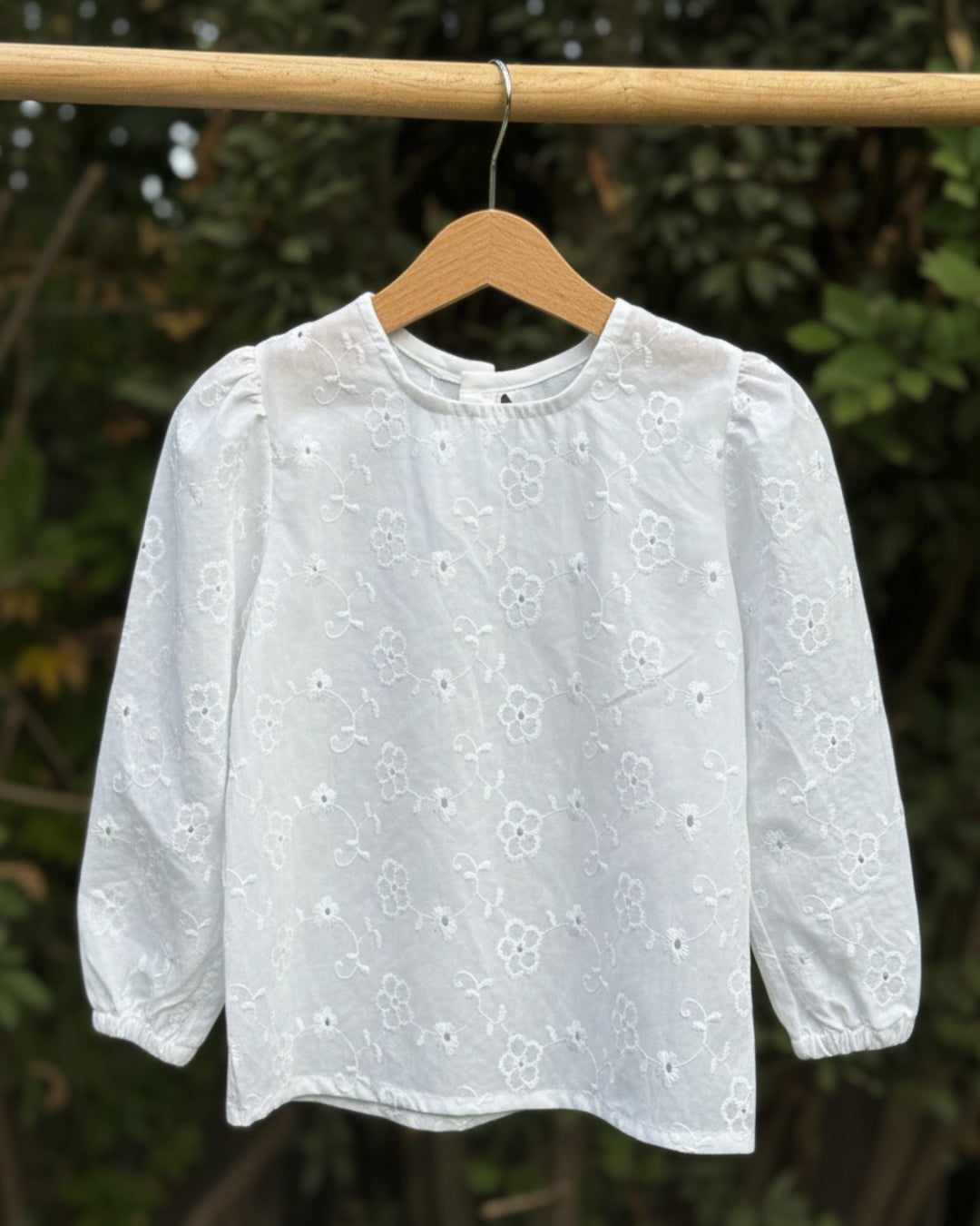 Blusa blanca Kankla de manga larga con bordado floral y elástico en puños. Cierre de dos botones en la espalda.