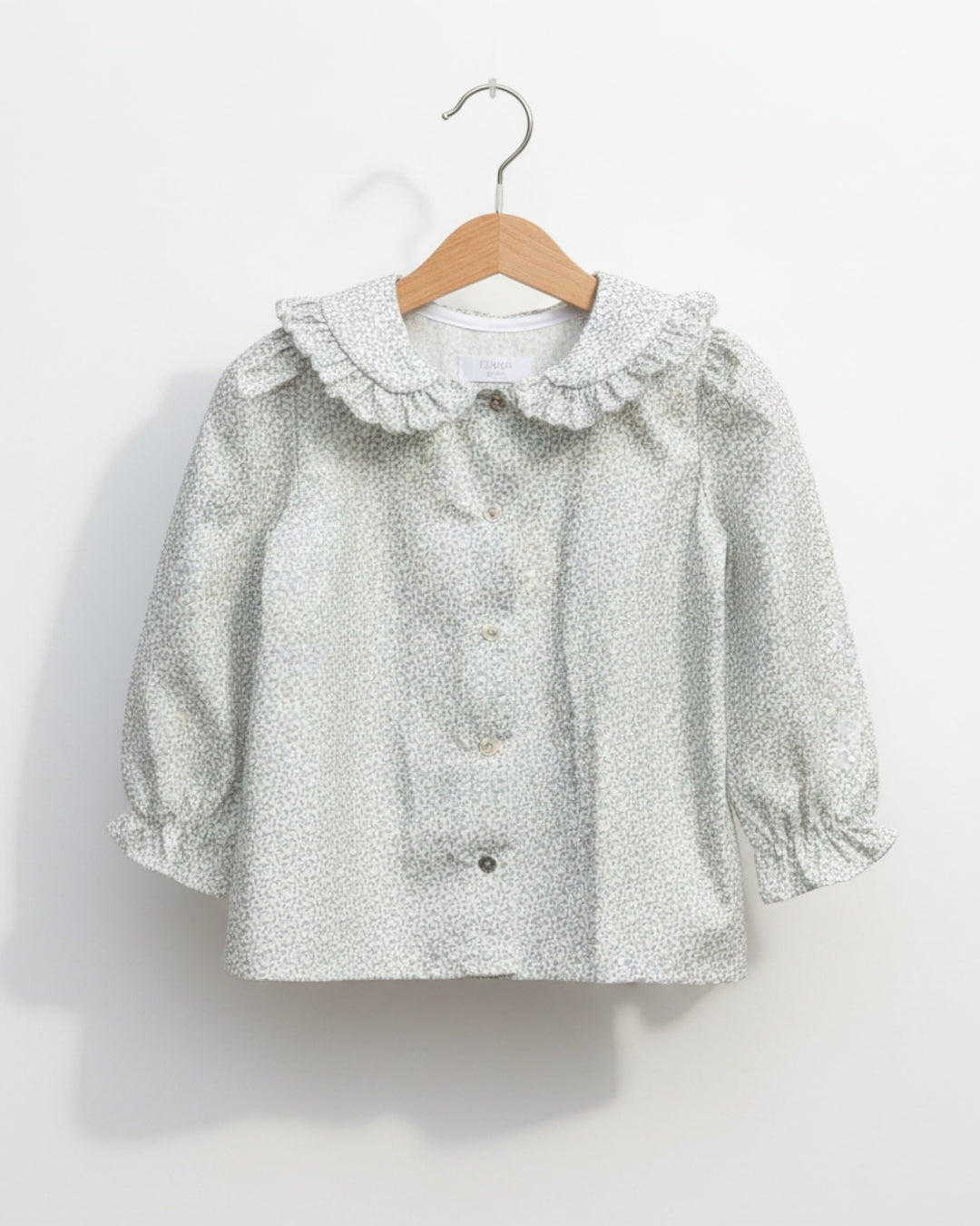 Blusa Kankla de algodón 100% con estampado de hojas grises, cuello volante y manga larga.