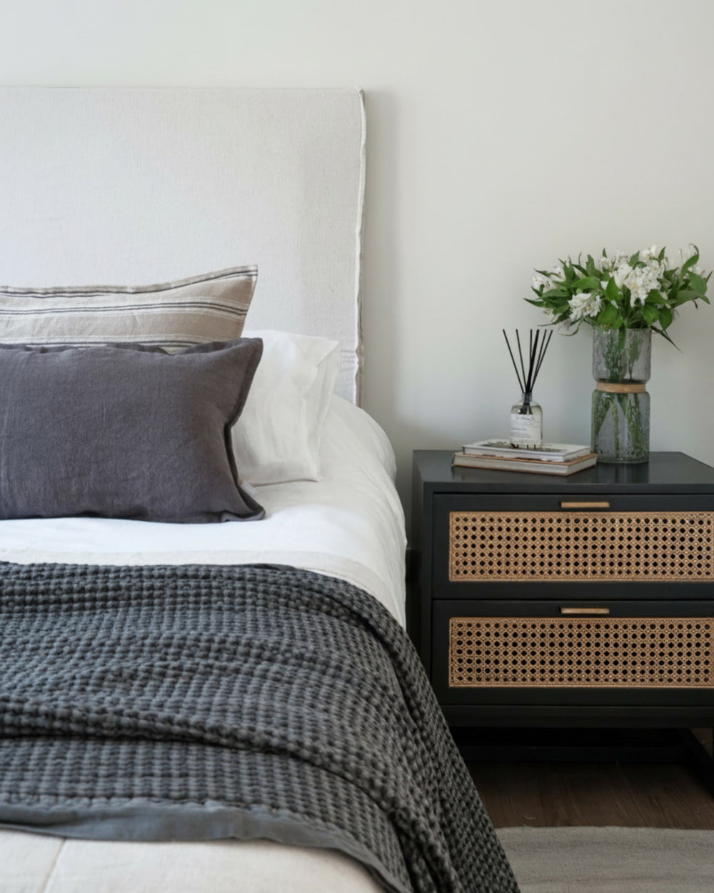 Funda de cojín Kankla de lino gris oscuro con borde de pestaña sobre una cama decorada en un dormitorio moderno.