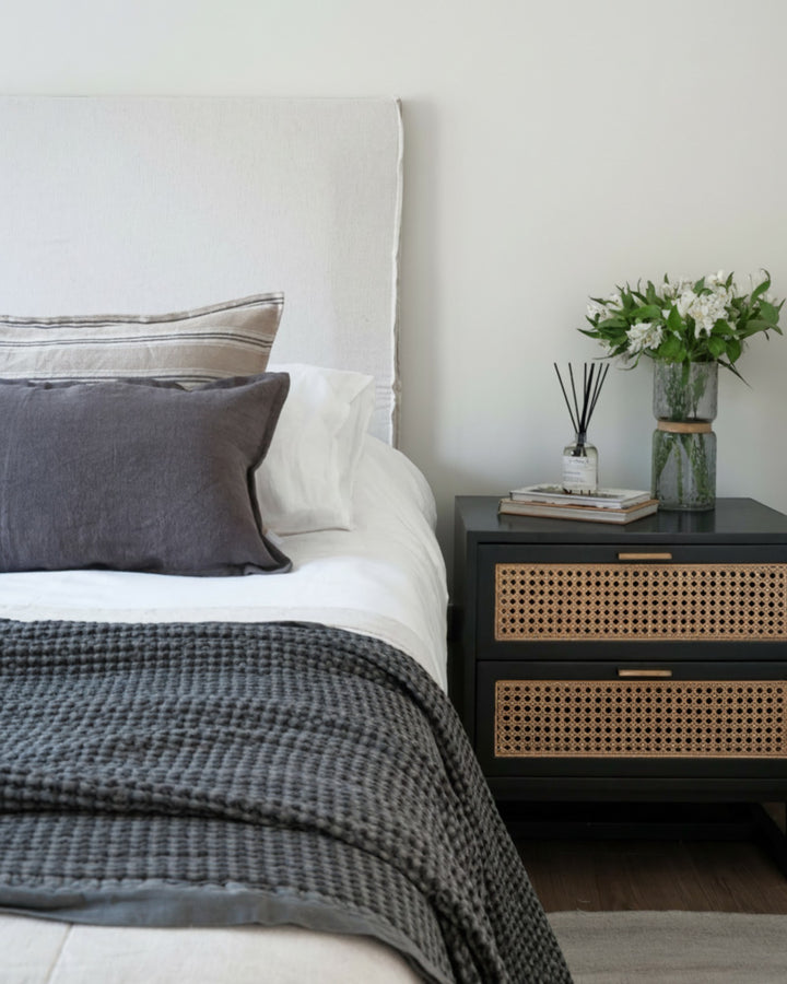 Funda de cojín Kankla de lino gris oscuro con borde de pestaña sobre una cama decorada en un dormitorio moderno.
