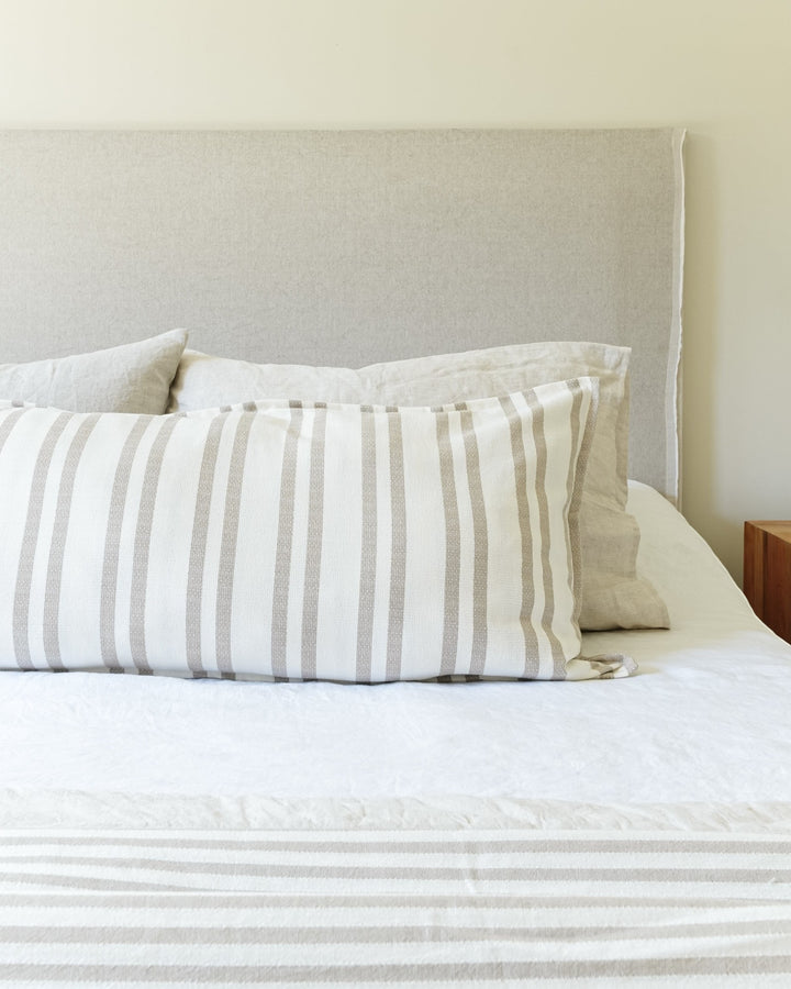 Funda de cojín Kankla Mónaco Beige de algodón con diseño de rayas sobre una cama con cabecero neutro