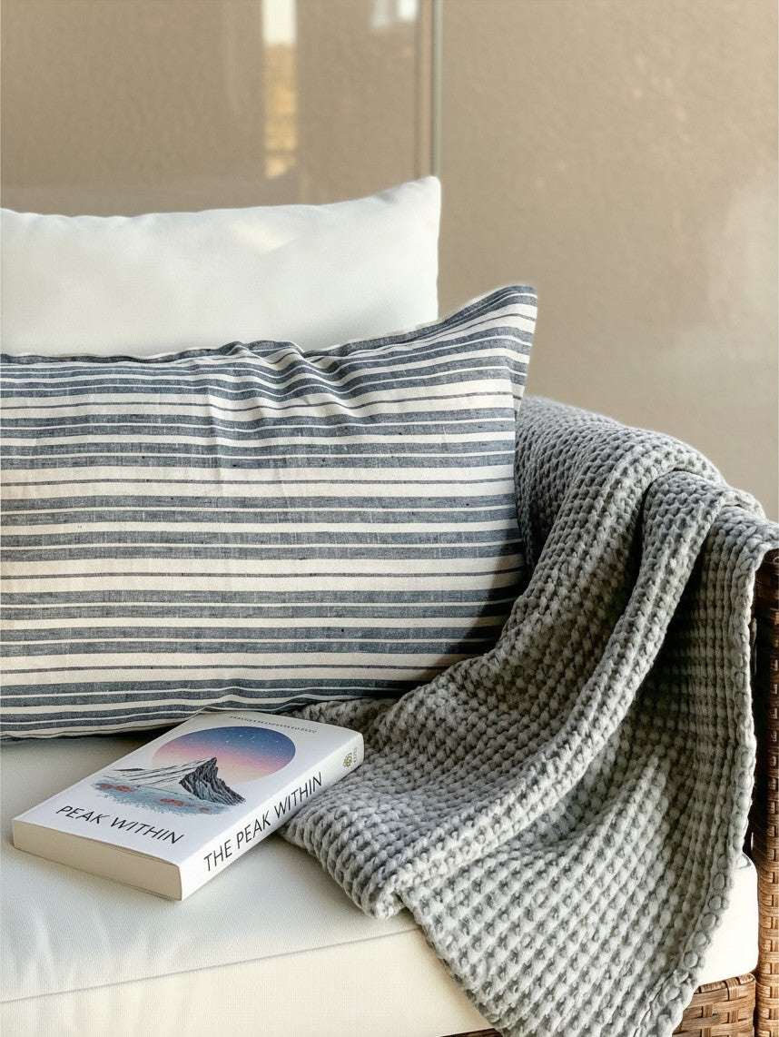 Funda de cojín Mykonos de Kankla en lino natural con rayas horizontales azules y blancas sobre un sofá