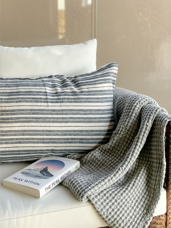 Funda de cojín Mykonos de Kankla en lino natural con rayas horizontales azules y blancas sobre un sofá