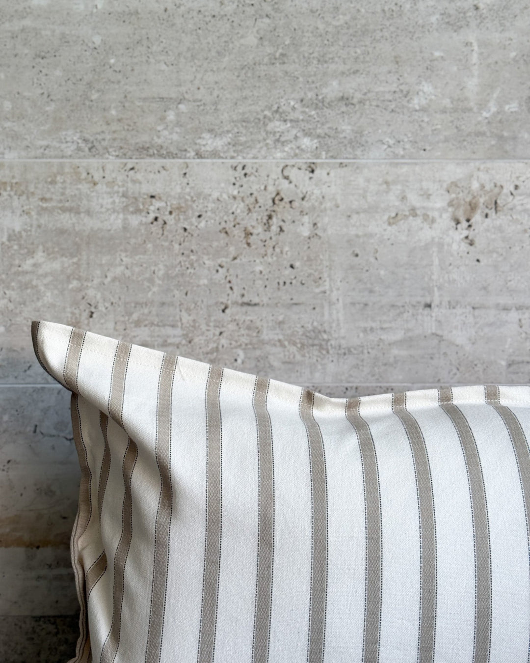 Funda de cojín Kankla Niza Beige de algodón con diseño de rayas verticales sobre fondo de piedra natural
