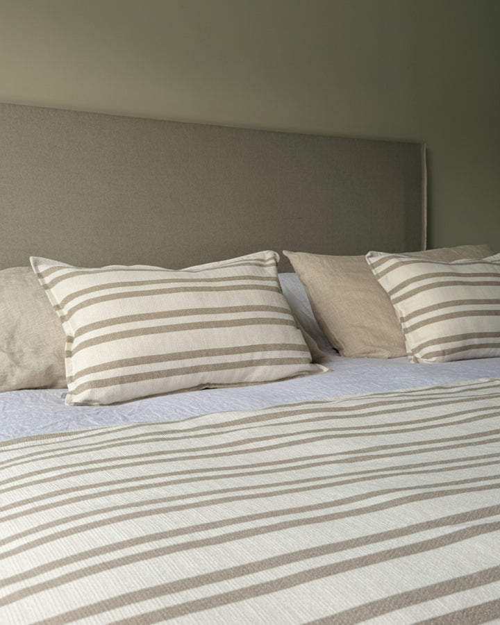 Piecera Kankla Mónaco beige reversible de algodón con líneas y reverso de lino sobre cama con cojines a juego