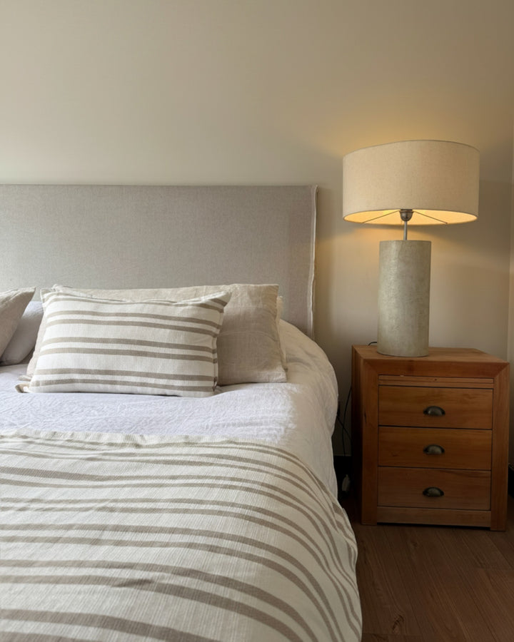 Piecera reversible Kankla Mónaco beige de algodón y lino con diseño de líneas sobre cama en dormitorio acogedor