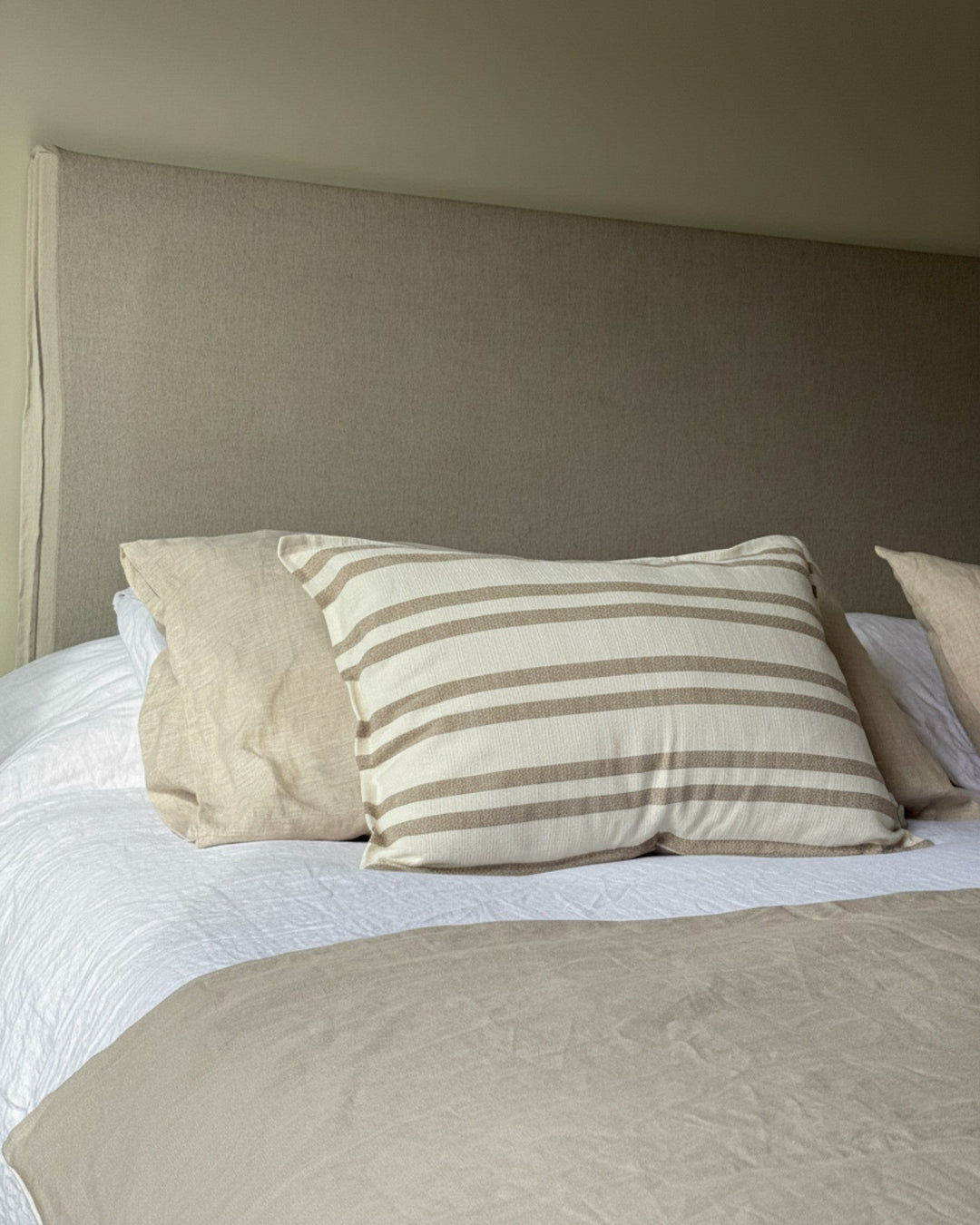 Piecera Kankla Niza reversible en lino greige y algodón a rayas sobre cama con almohadones neutros