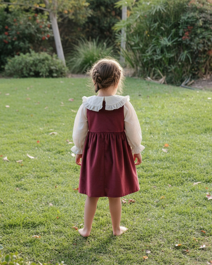 Kankla Vestido rojo sin mangas de terciopelo con cuello de encaje y falda fruncida. Niña de espaldas en el césped.