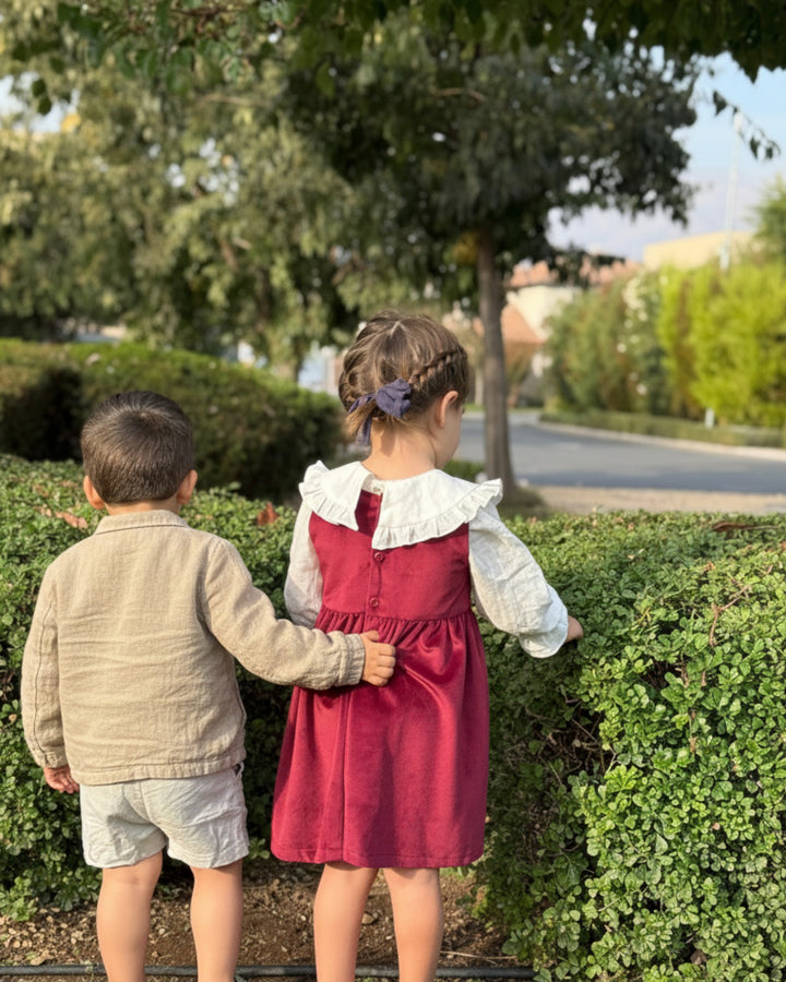 Vestido rojo sin mangas de terciopelo Kankla con cuello blanco y botones en la espalda. Niña de espaldas.